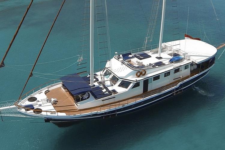 white motor sailing yacht with two masts anchored in clear turquoise Mediterranean waters