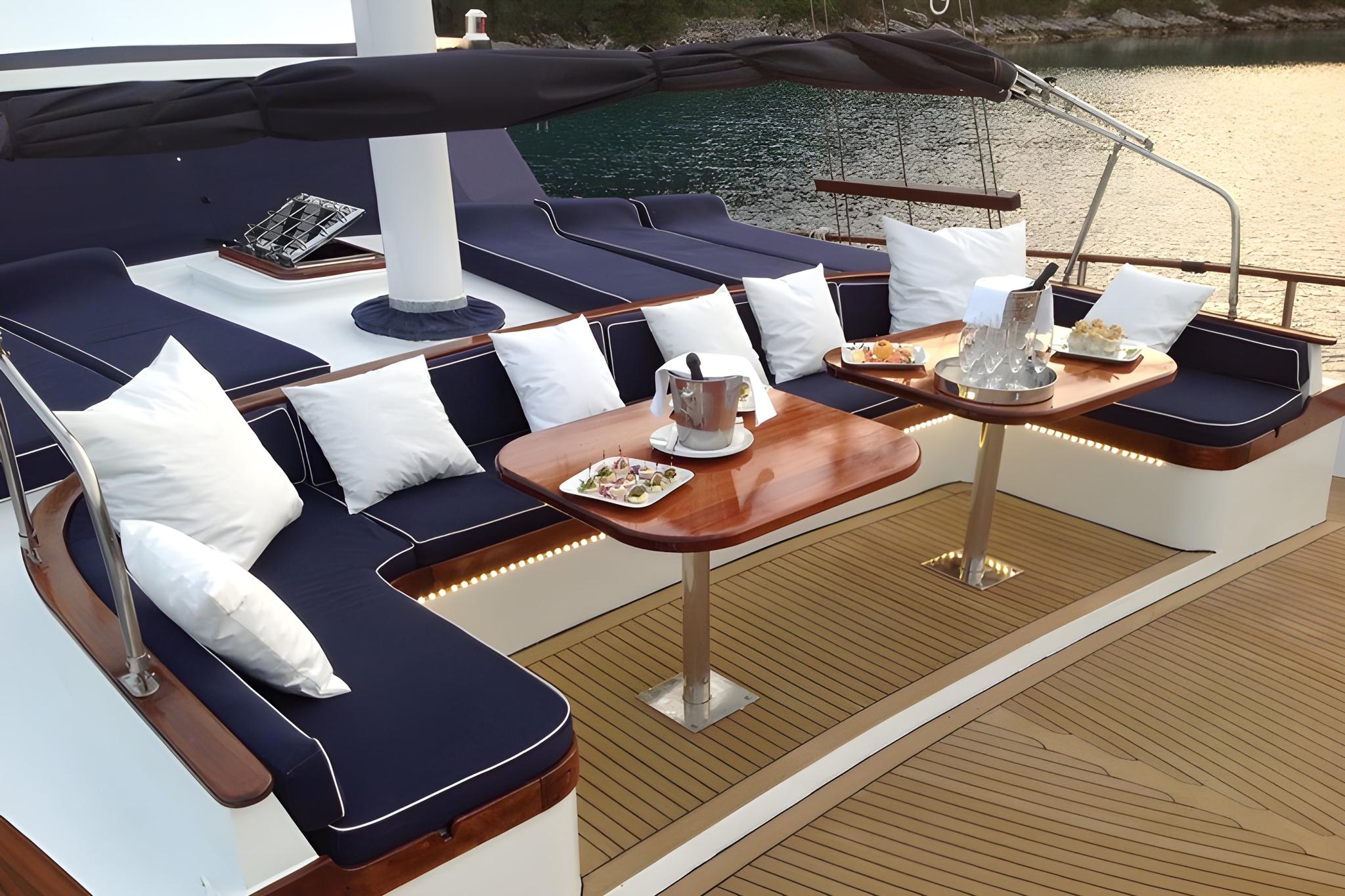 yacht aft deck with navy blue seating, teak dining table, and white cushions