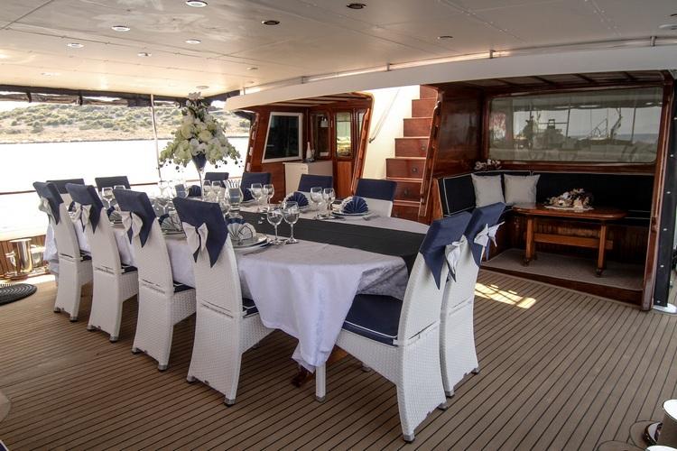 yacht aft deck dining area with white wicker chairs and formal table setting under awning