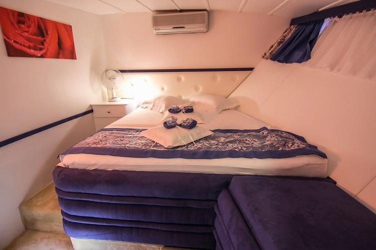 yacht cabin interior with double bed, white bedding, towels, porthole window and air conditioning
