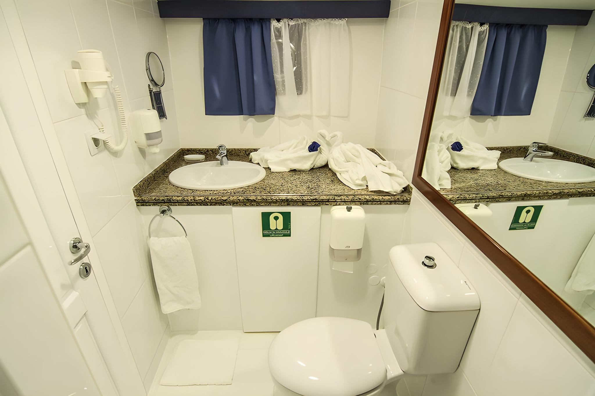 yacht bathroom featuring granite countertop vanity, oval sink, large mirror and white toilet