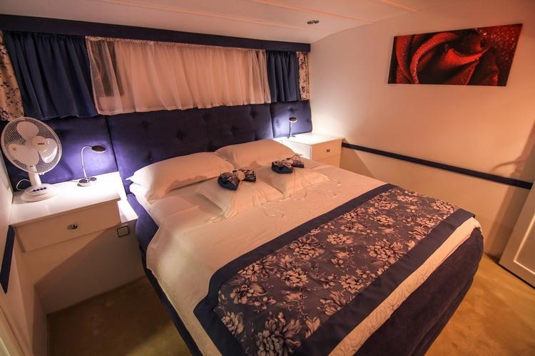 yacht guest cabin with double bed, nautical curtains, bedside reading lights and decorative wall art