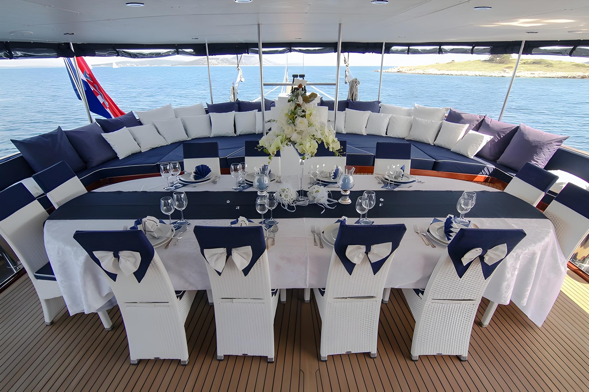 yacht aft deck with formal dining table, white chairs, and curved seating area