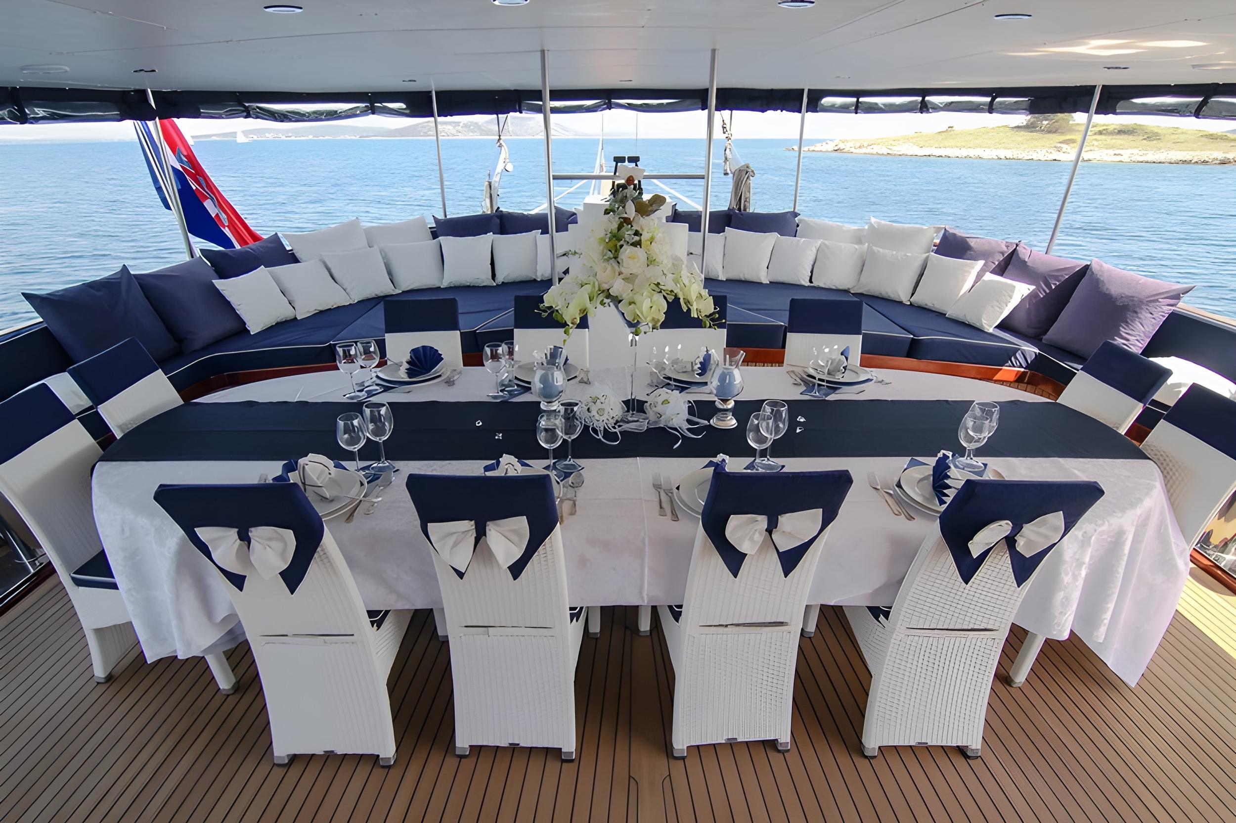 yacht aft deck with formal dining table, white chairs, and curved seating area
