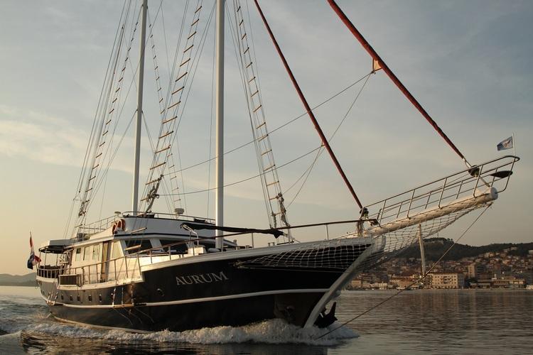AURUM luxury gulet sailing yacht underway with full sails and coastal town backdrop
