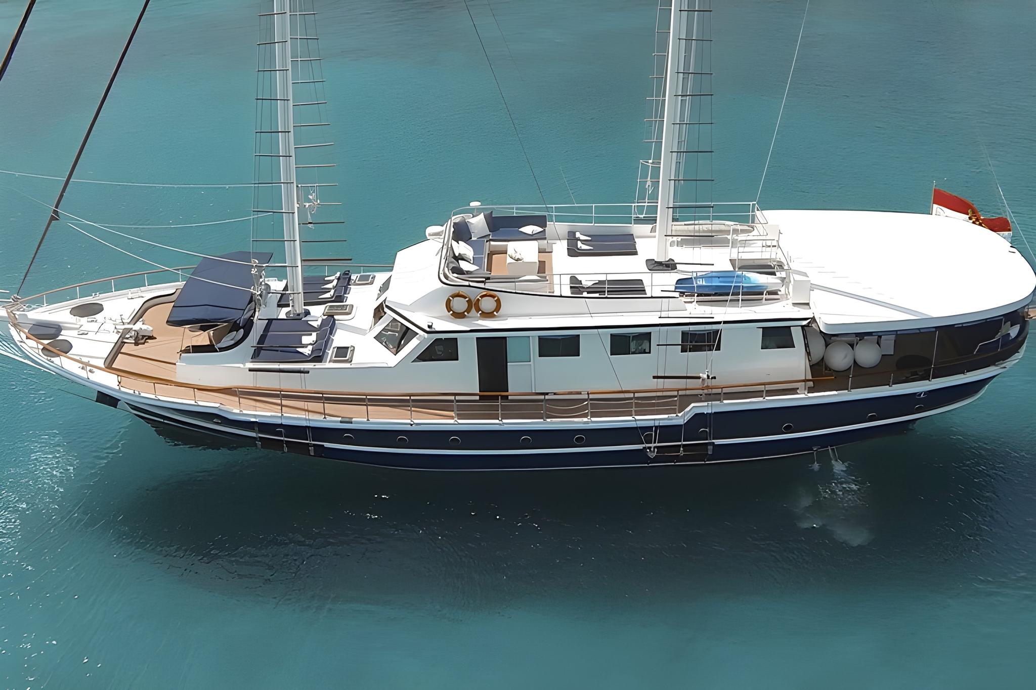 Traditional gulet yacht with white superstructure and navy blue hull anchored in turquoise waters