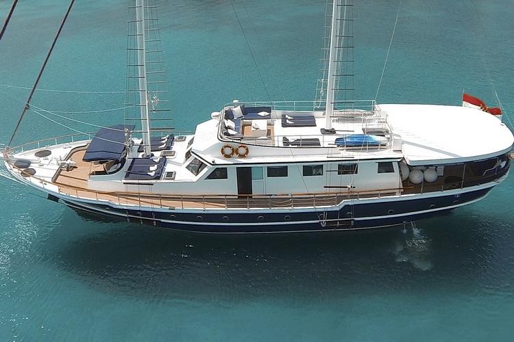 Traditional gulet yacht with white superstructure and navy blue hull anchored in turquoise waters