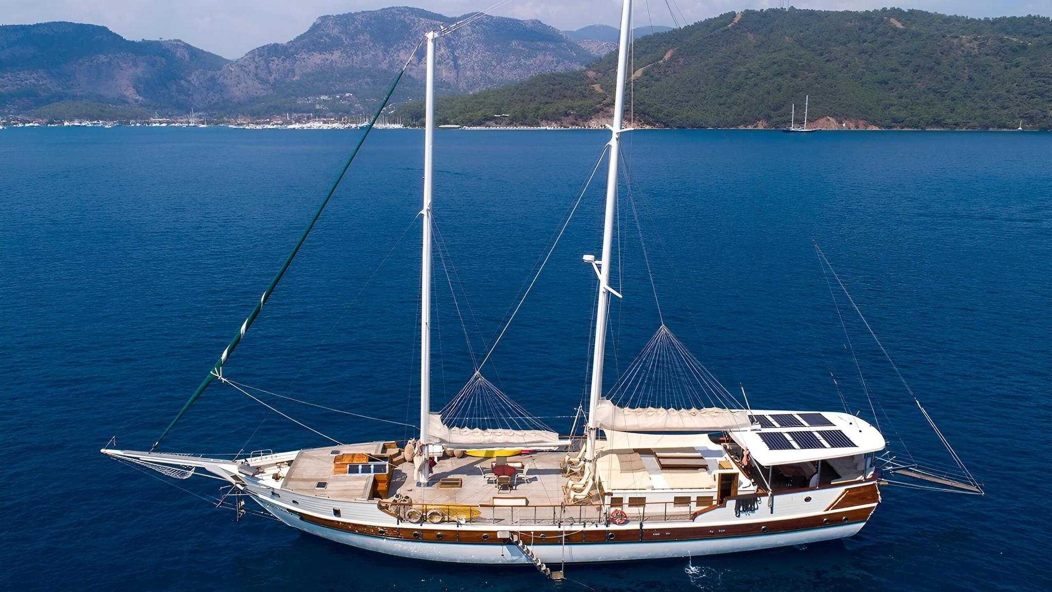 Traditional wooden gulet yacht with two masts anchored in calm blue Mediterranean waters with mountainous coastline