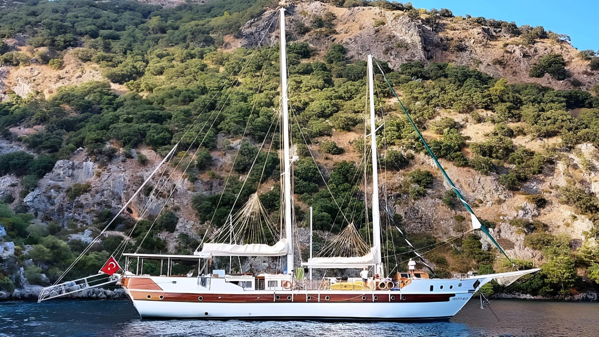 Traditional wooden gulet with two masts anchored in secluded Mediterranean bay with rocky coastline