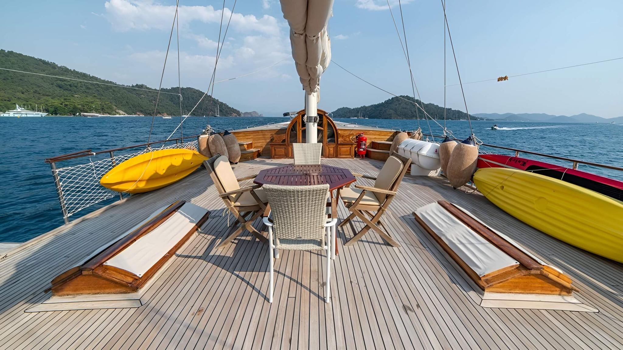 yellow and red kayaks stored on foredeck of traditional wooden sailing yacht with dining area