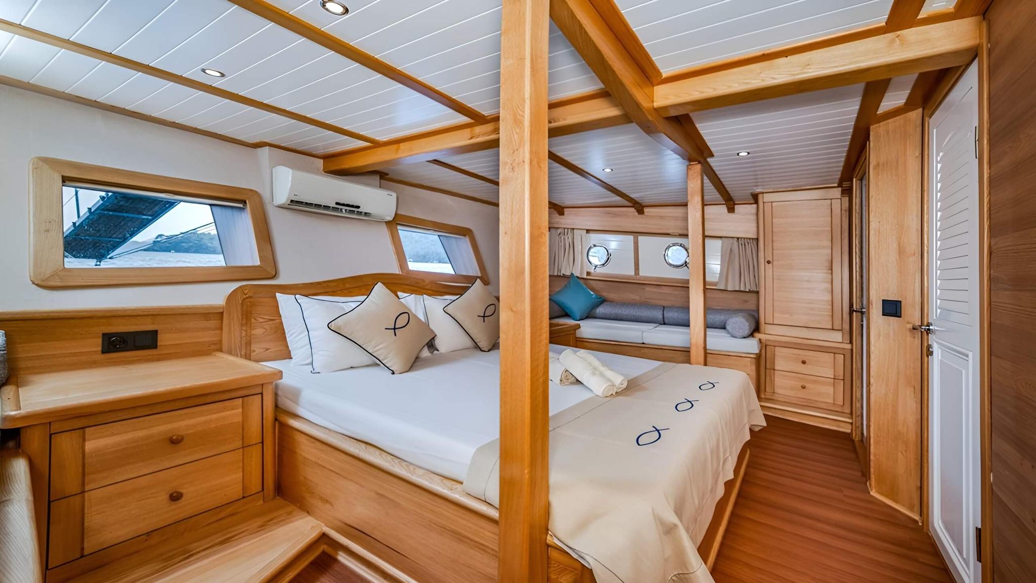 yacht guest cabin with double bed, wood paneling, windows and seating nook