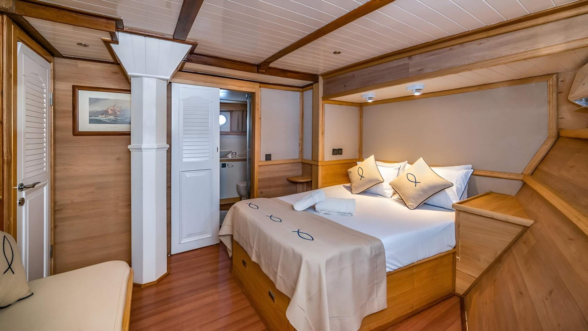 yacht guest cabin featuring double bed with white linens, wooden finishes, and en-suite bathroom door