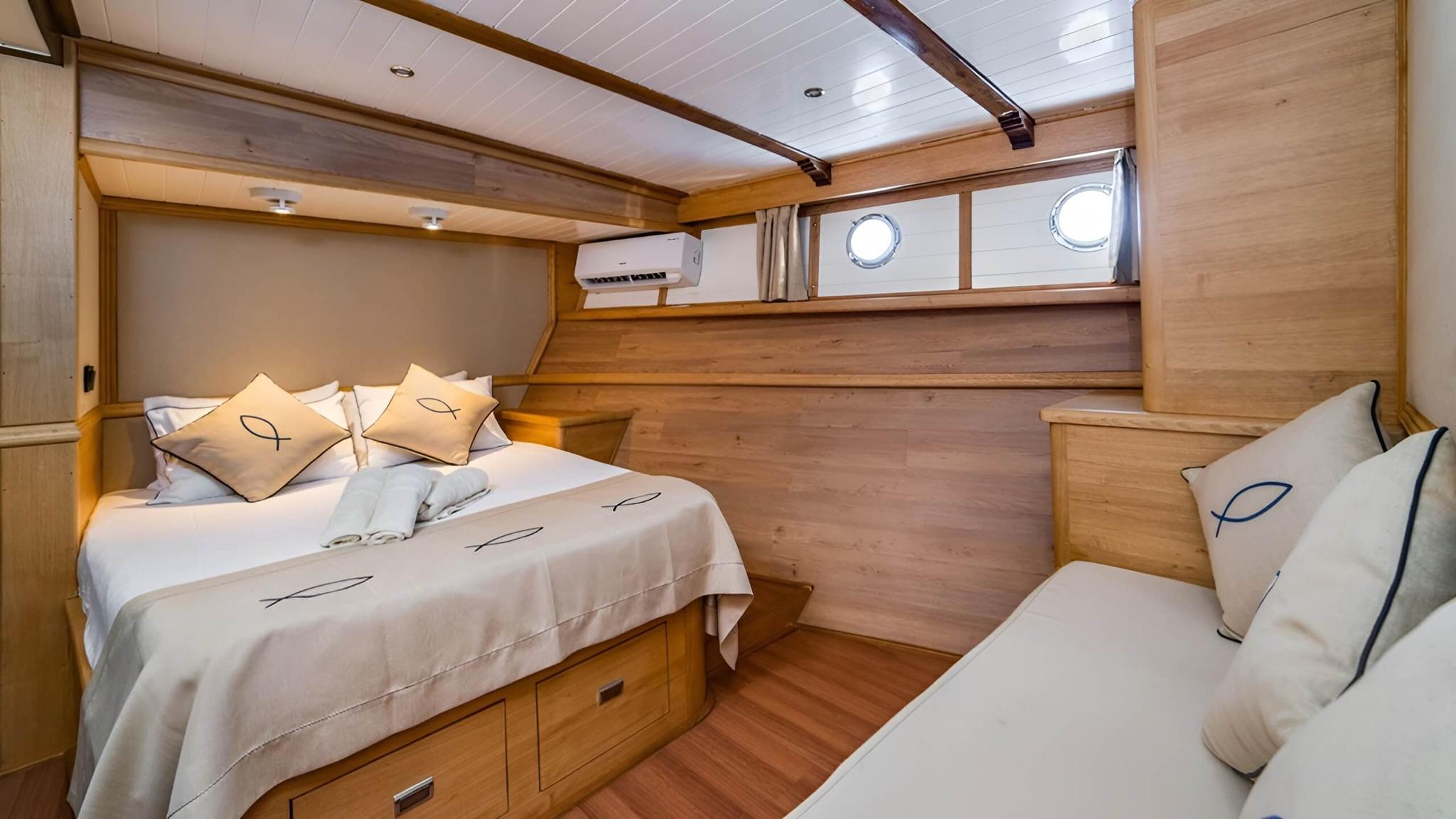 yacht guest cabin featuring double bed with storage drawers and single berth with portholes