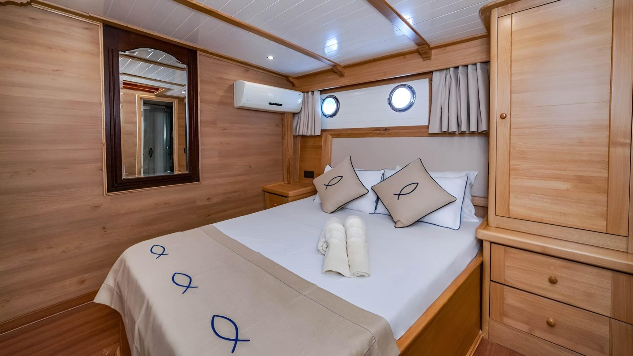 yacht guest cabin featuring double bed with white linens, natural wood paneling, portholes, and built-in wardrobe