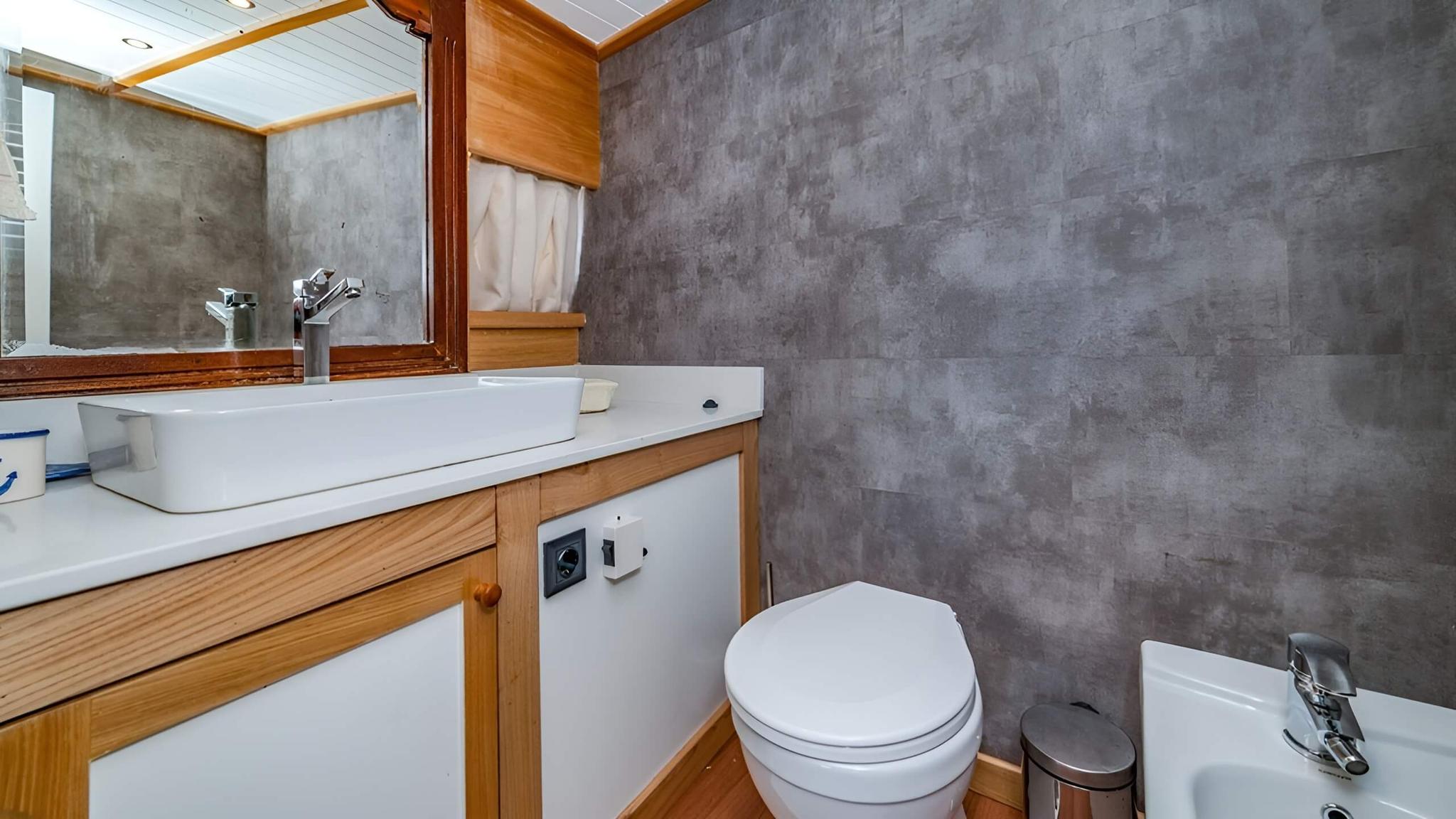 yacht bathroom featuring white vessel sink on wooden vanity with toilet and gray textured walls