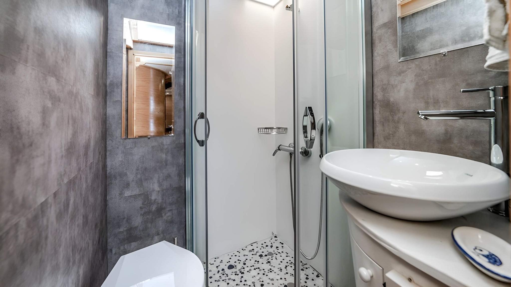 yacht bathroom with white toilet, round basin, glass shower door and grey marble walls