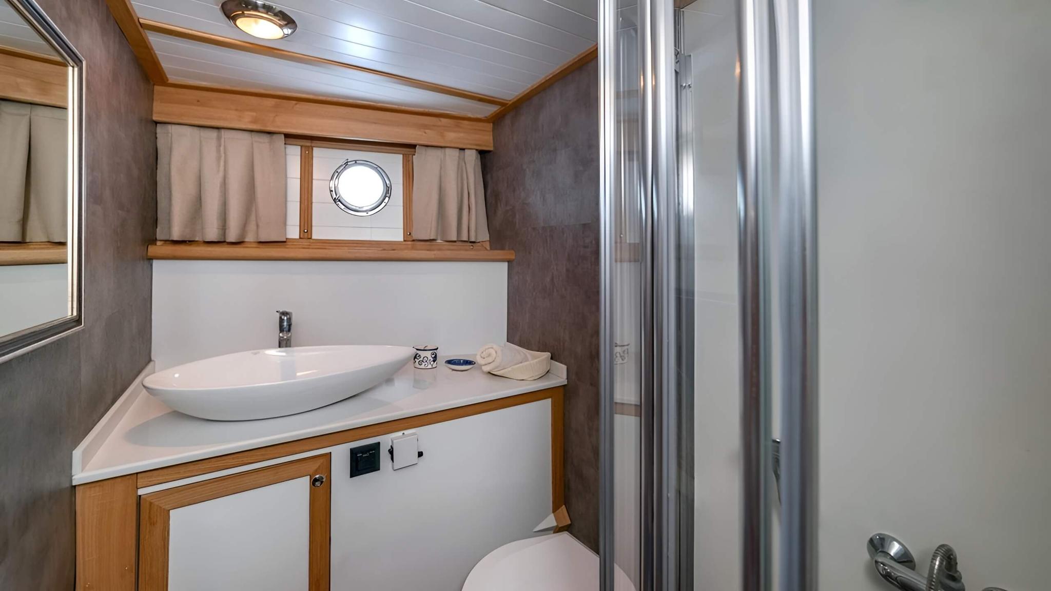 yacht guest bathroom featuring white vessel sink, porthole window, and glass shower enclosure