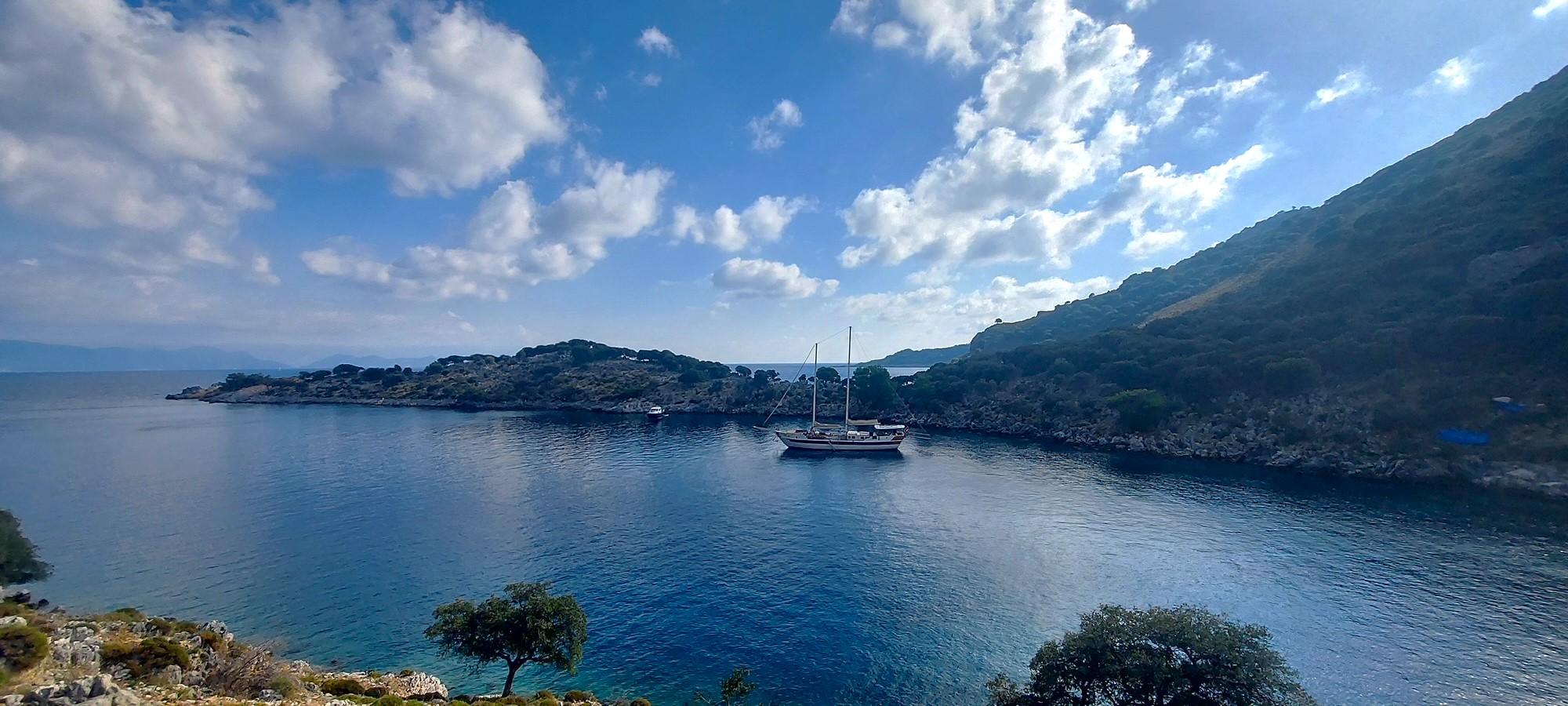 Traditional wooden gulet yacht anchored in pristine blue bay surrounded by rocky coastline