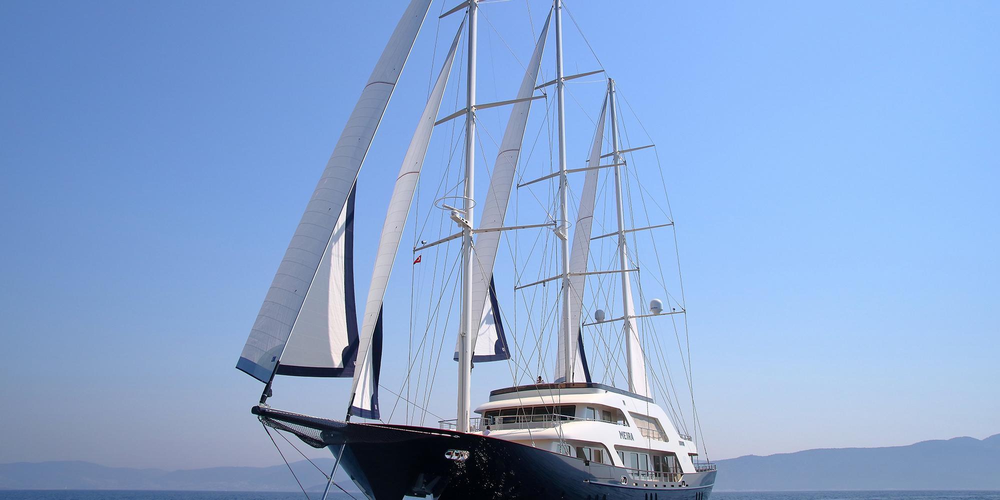 luxury sailing yacht with multiple white sails raised cruising on calm blue waters