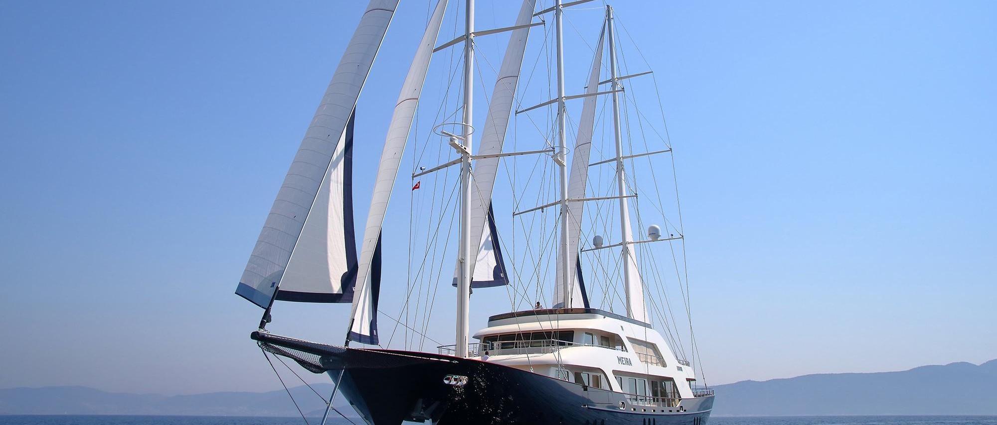 White luxury sailing yacht with multiple sails deployed cruising on calm blue water