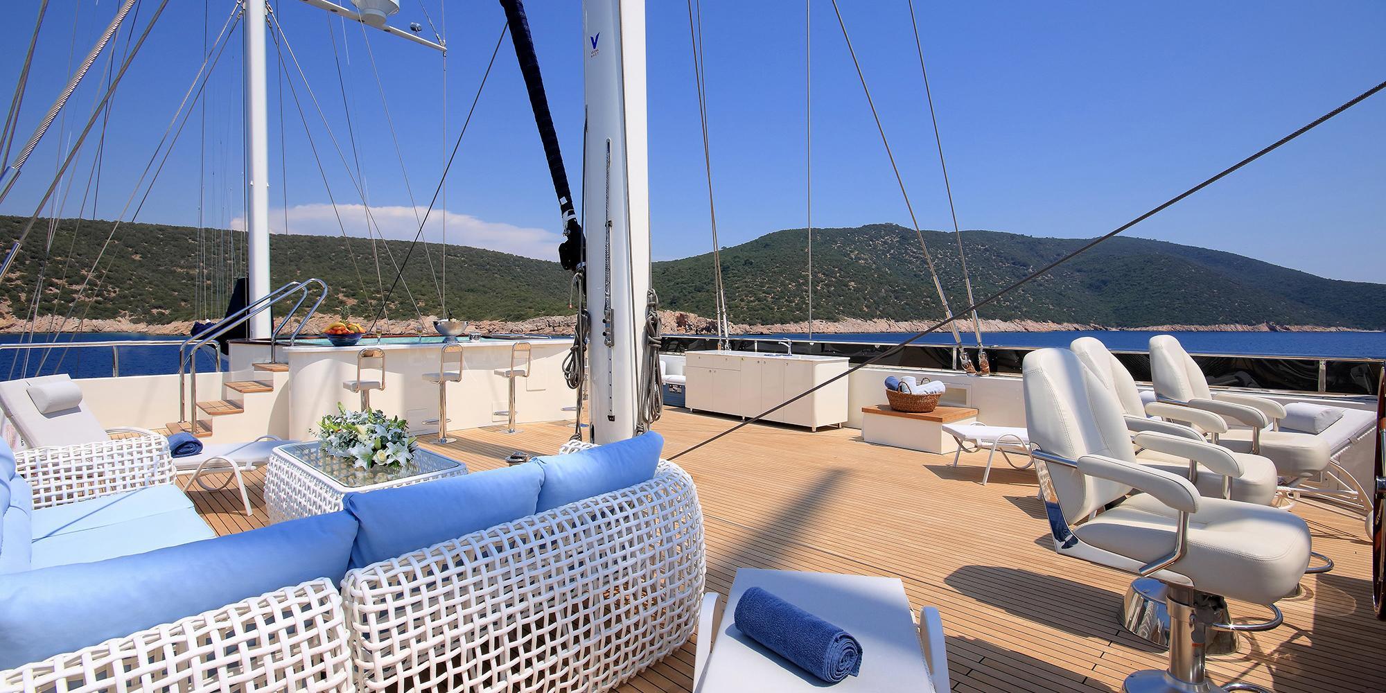 gulet main deck with white wicker lounge furniture, blue cushions, and teak decking