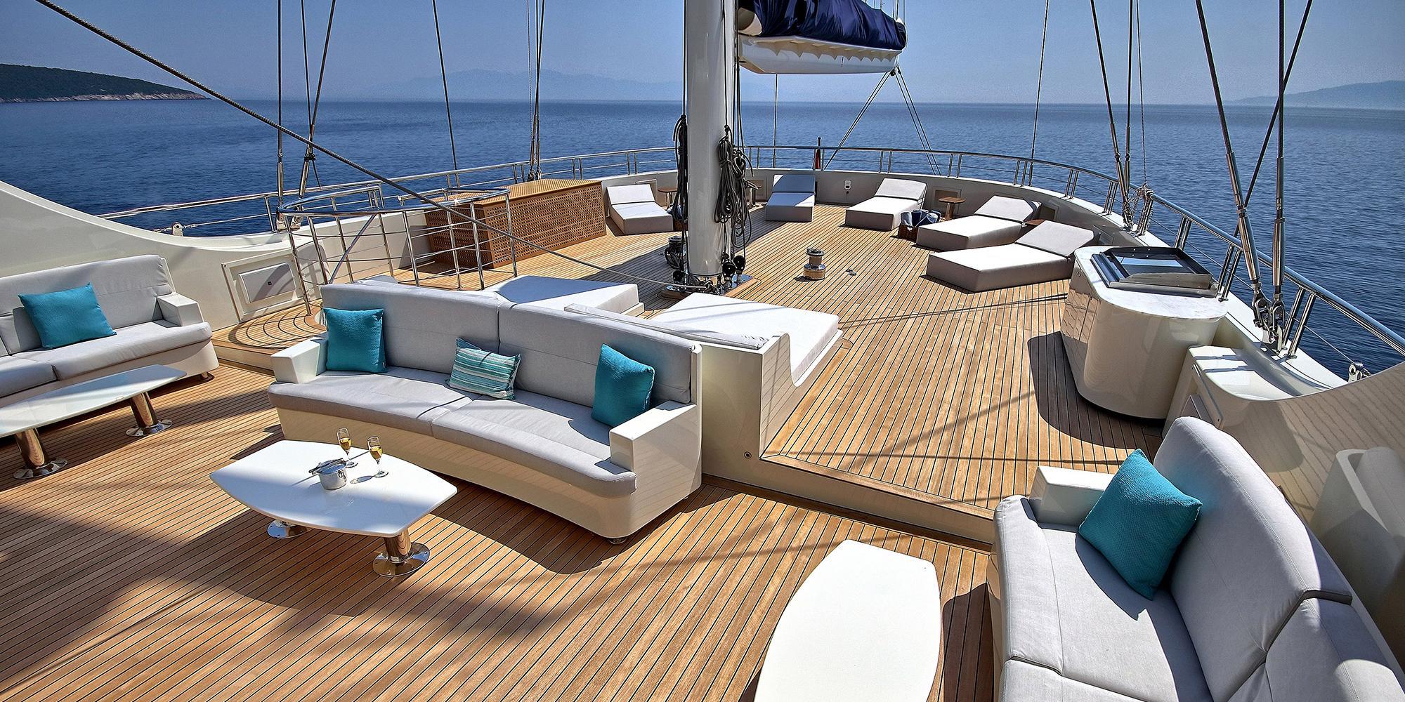 yacht main deck lounge area with white cushioned sofas, turquoise pillows, and teak decking