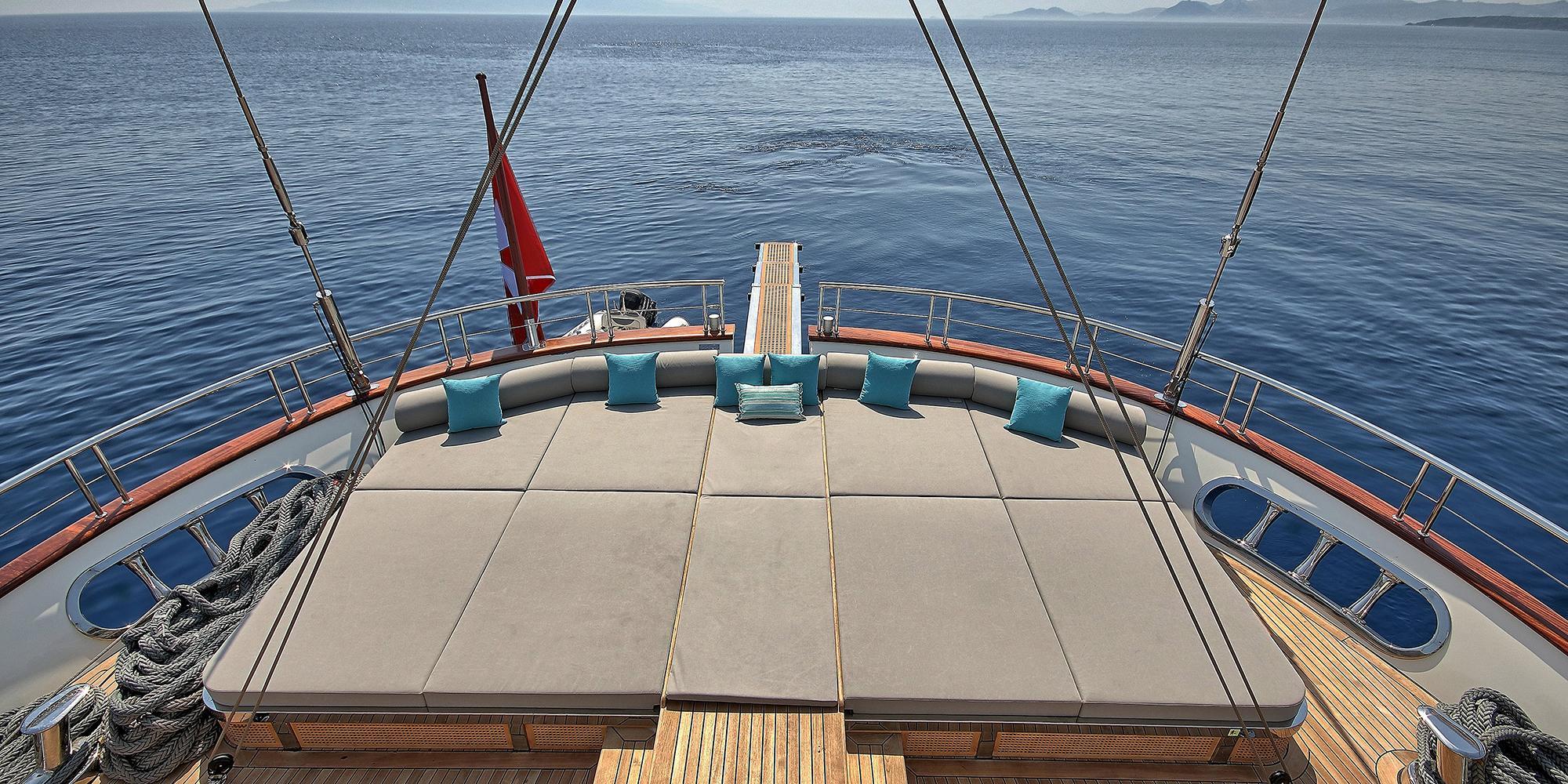 gulet bow sun deck with curved bench seating, turquoise cushions and sailing rigging