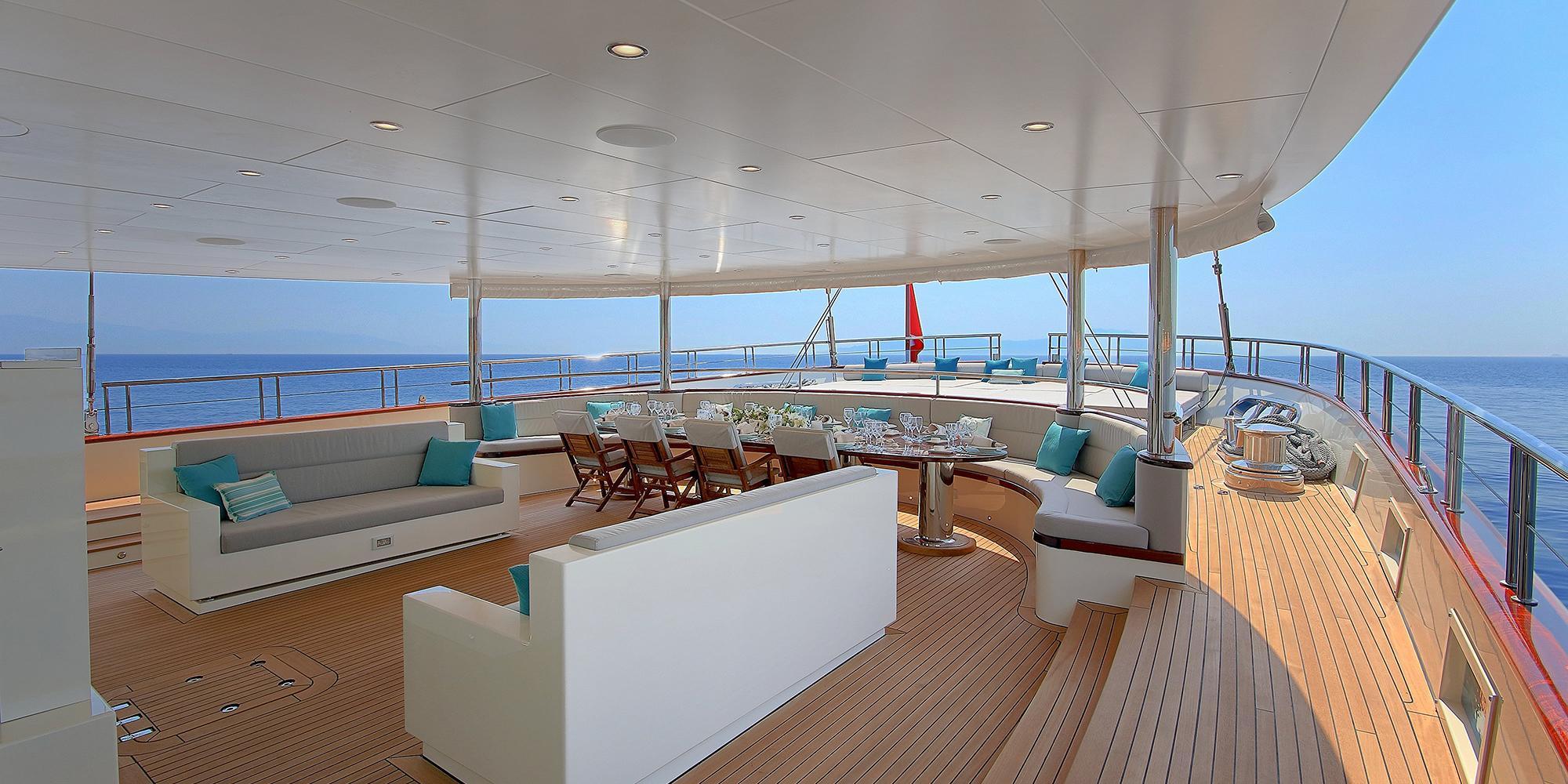 yacht upper deck with curved sofa seating, dining table, and panoramic ocean views