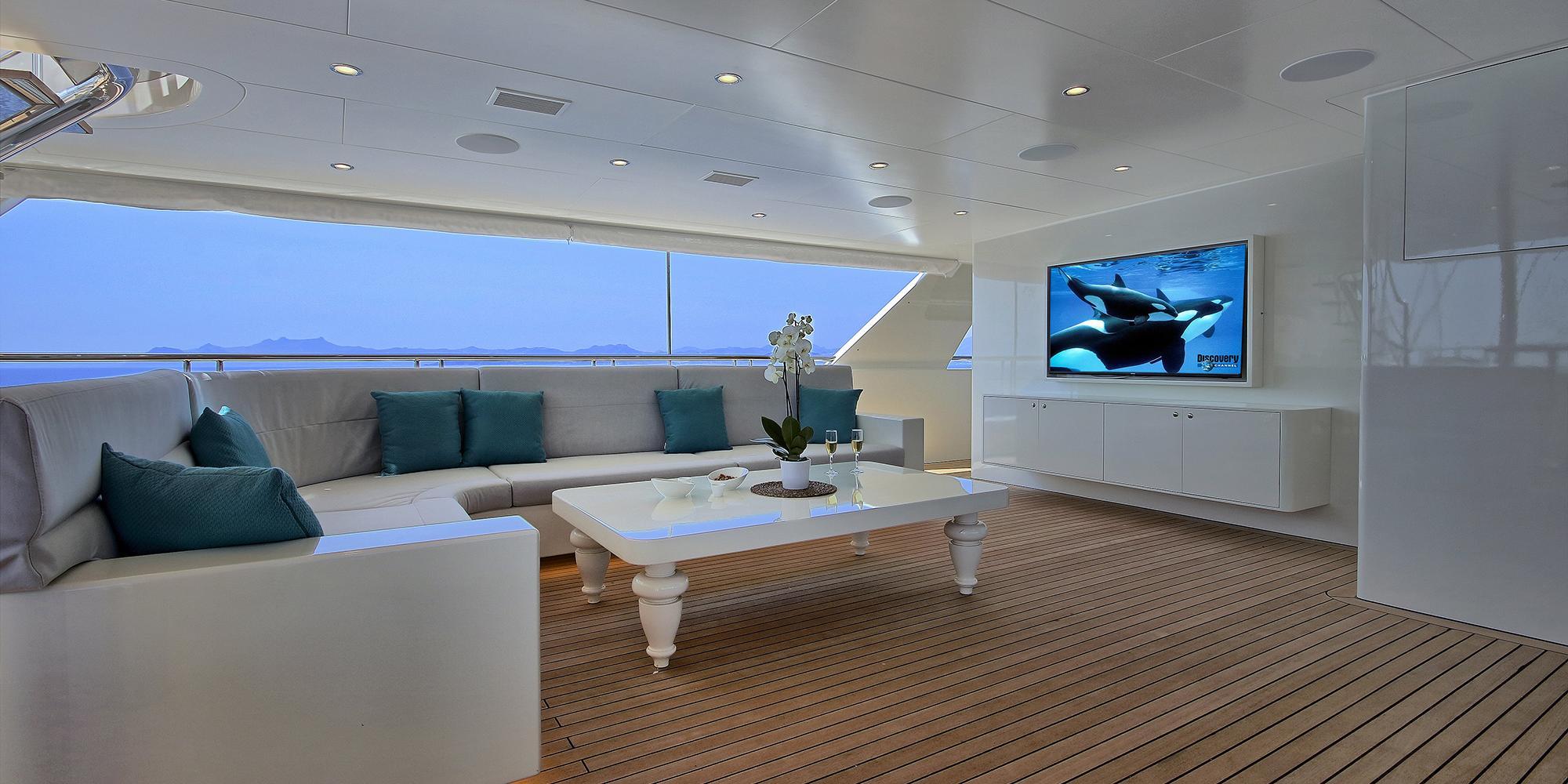 yacht cinema room with wall-mounted TV displaying marine life, white sectional seating and teak flooring