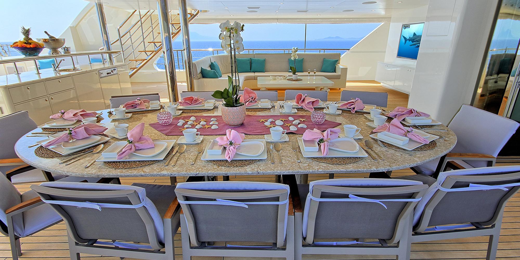 yacht aft deck dining area with oval table set for formal meal and seating lounge