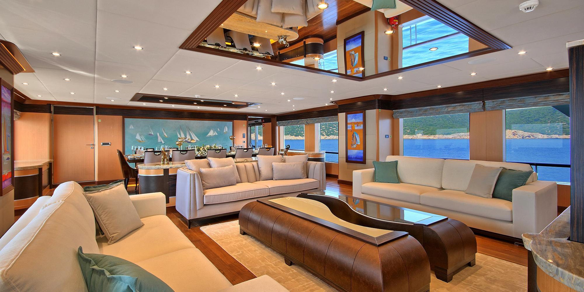 yacht main salon with cream sofas, brown leather ottoman, dining area and panoramic windows