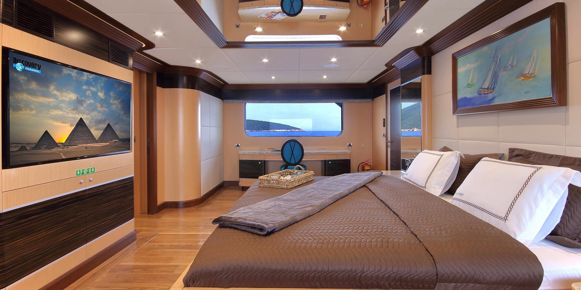 luxury yacht master cabin cinema room with large wall-mounted screen showing pyramids, king bed and panoramic windows