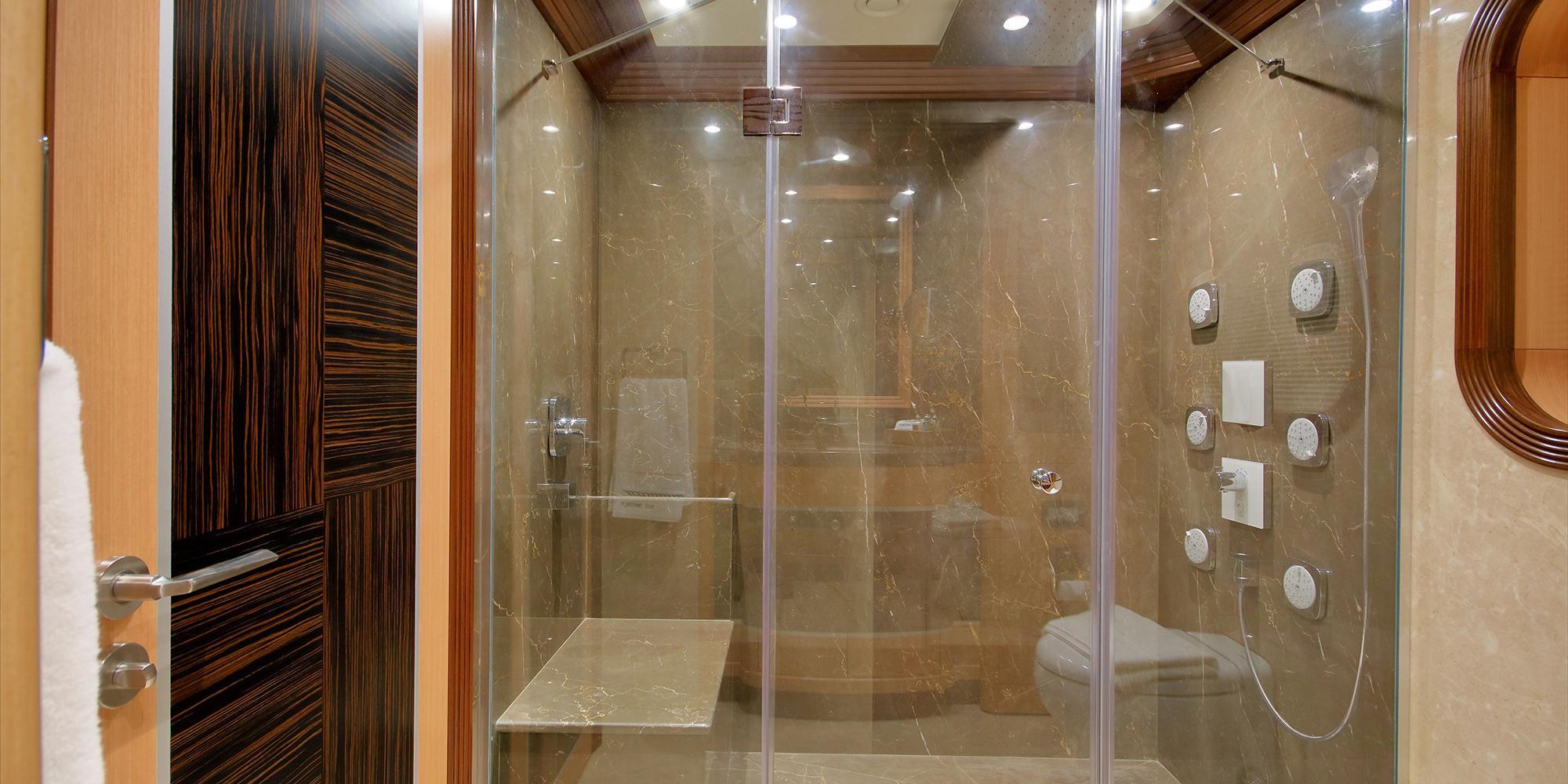 spacious yacht bathroom featuring marble-clad shower with glass doors and body jets
