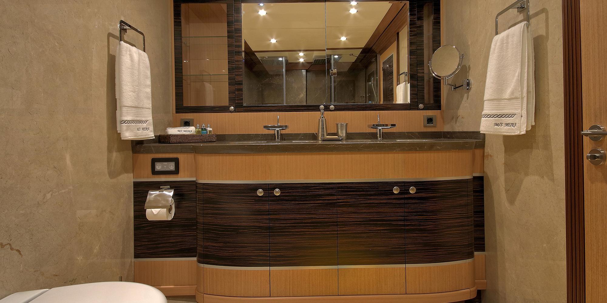 luxury yacht bathroom featuring curved double vanity with marble countertop and large mirror