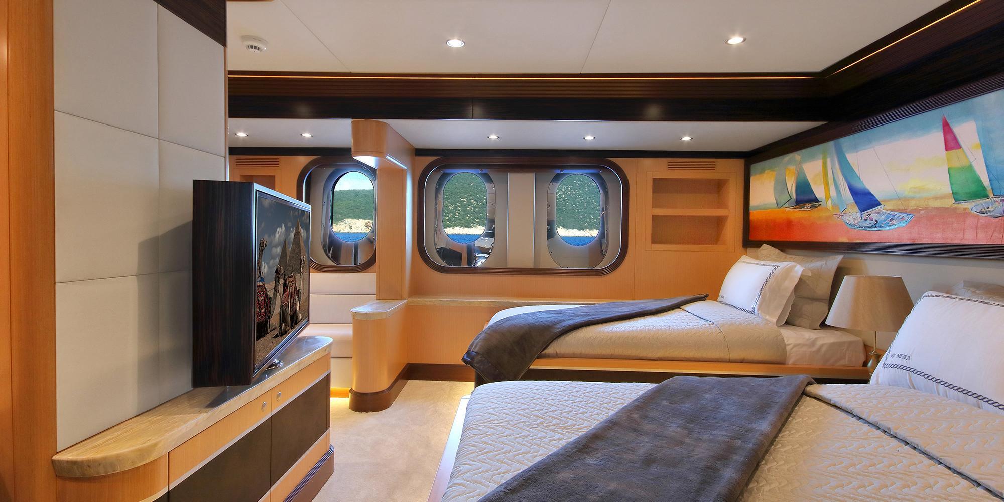 yacht guest cabin with two twin beds, three portholes, wall-mounted TV and sailing artwork