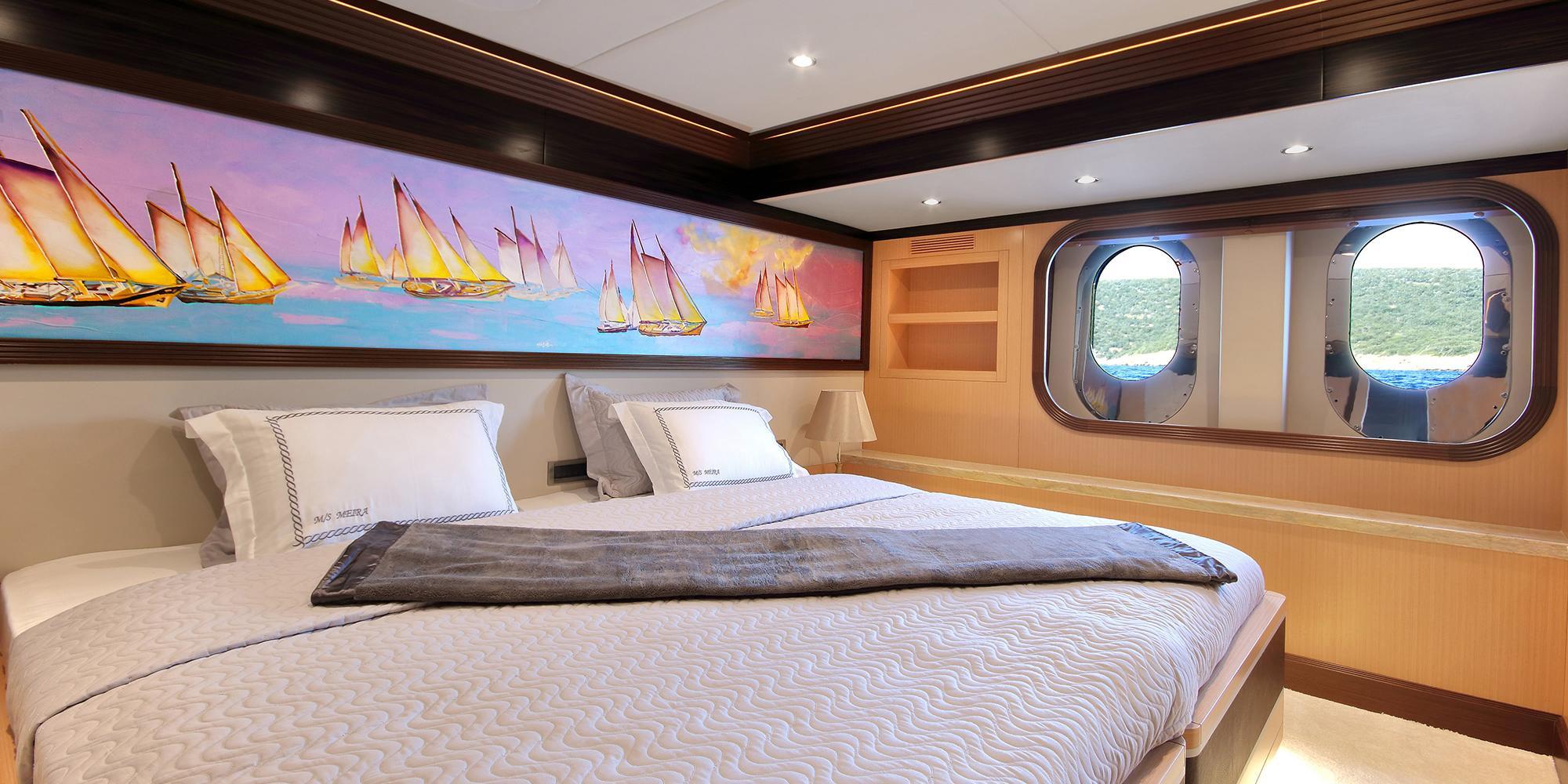 yacht cabin interior with double bed, nautical artwork, and two oval portholes