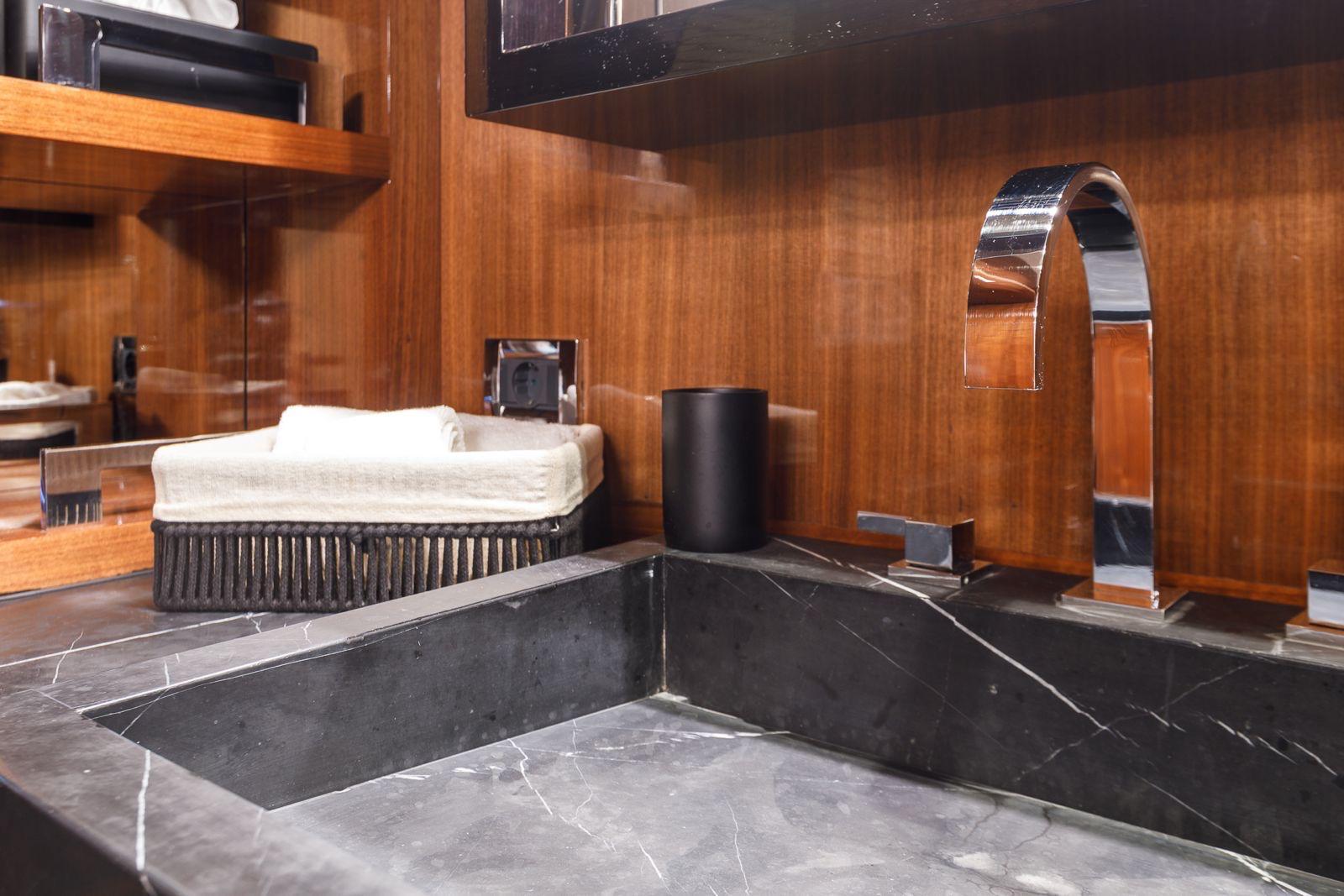 luxury yacht bathroom featuring black marble integrated sink with chrome faucet and warm wood paneling