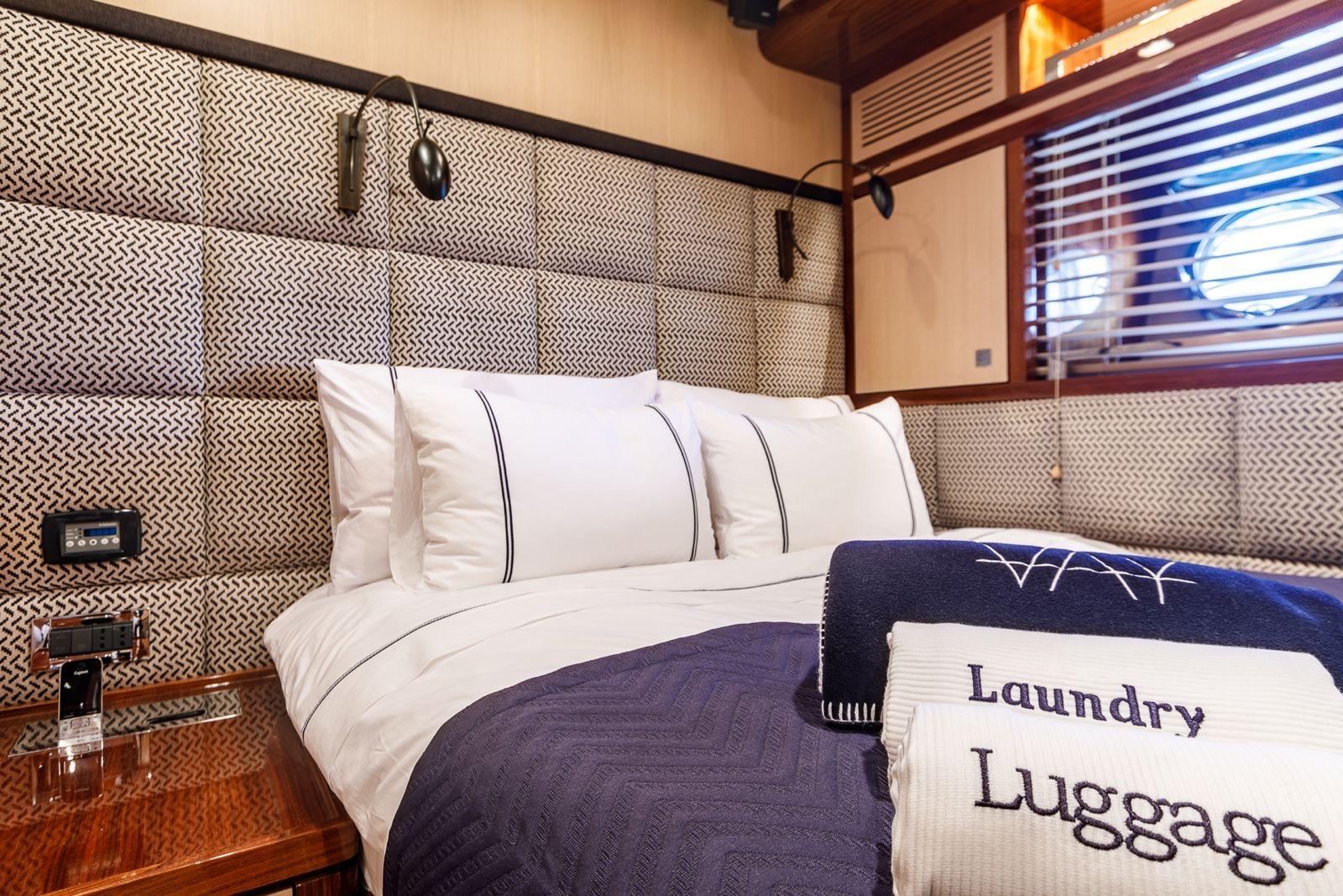 yacht cabin interior with double bed, white linens, blue throw blanket and laundry bag