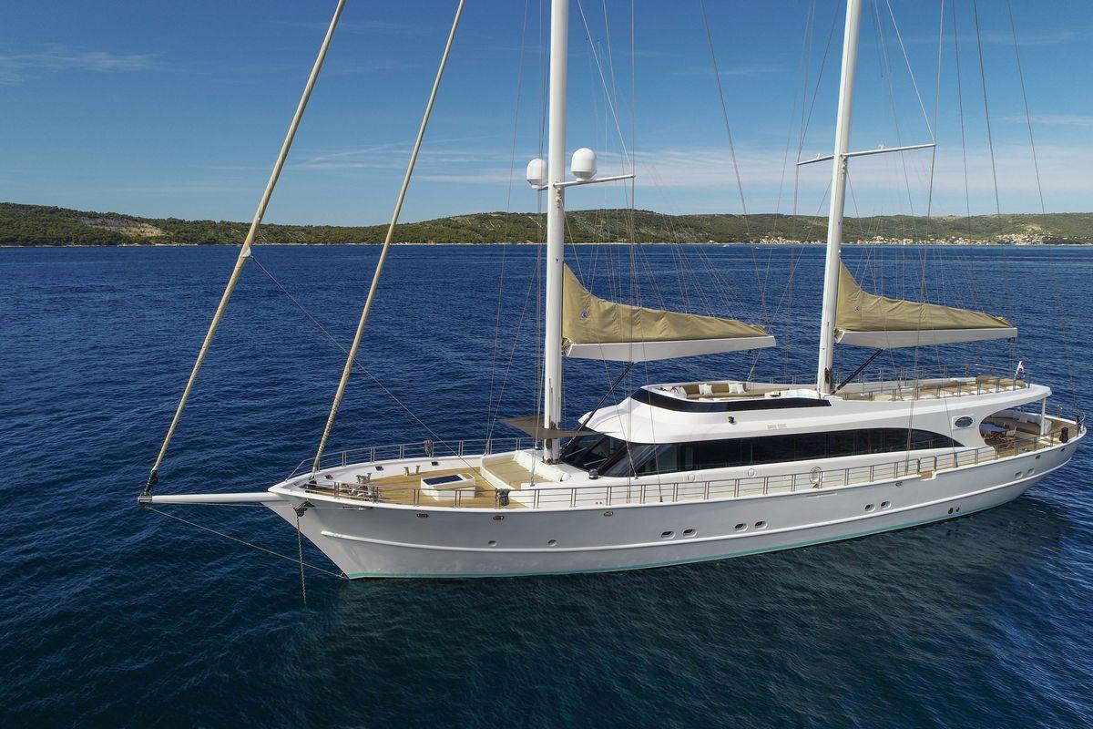 White luxury sailing yacht with two masts anchored near forested coastline