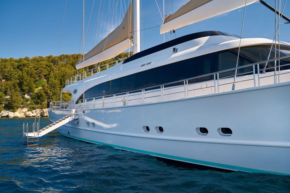 White luxury sailing yacht with blue hull stripe anchored in clear turquoise water