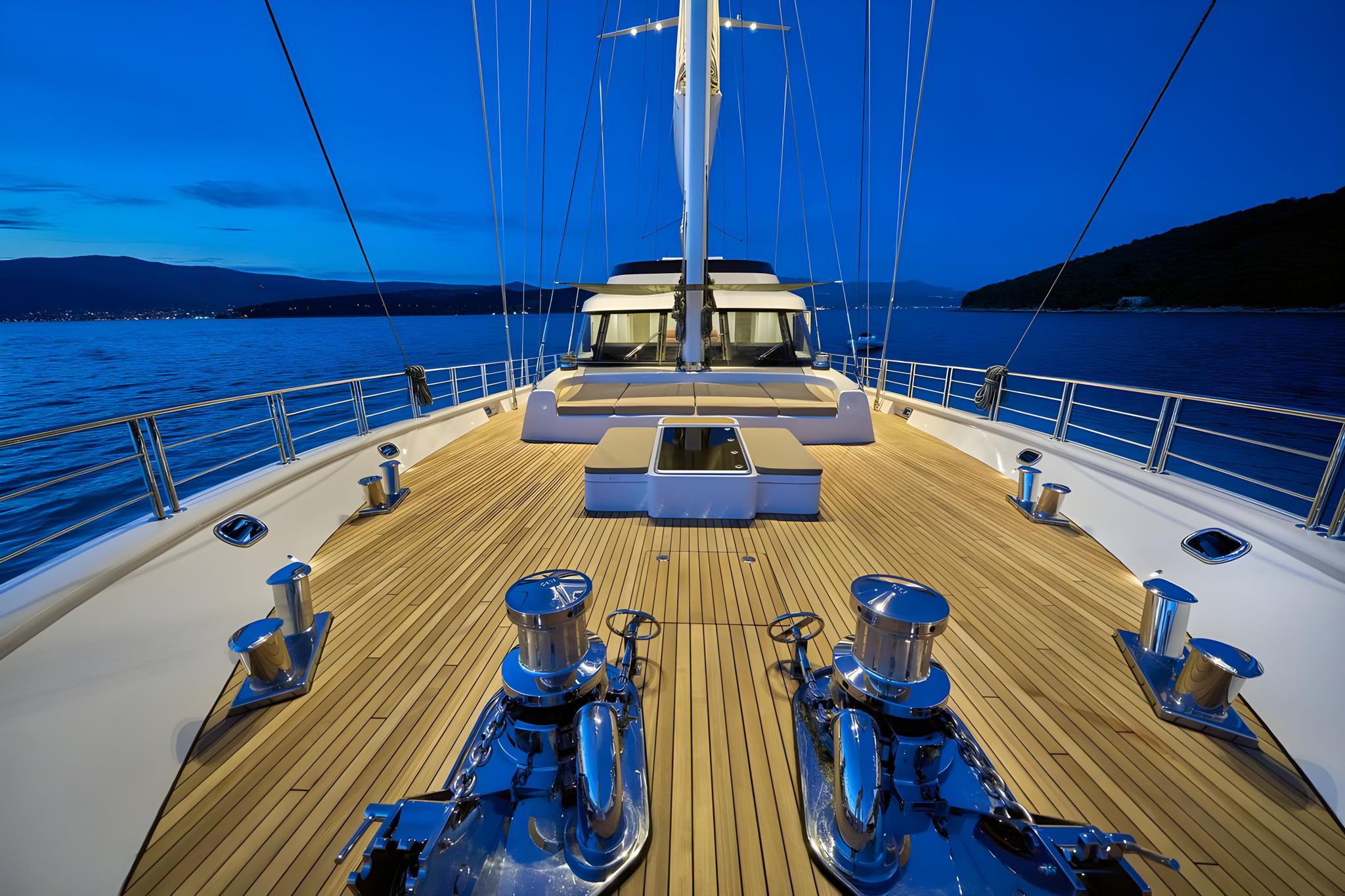 luxury yacht forward deck with teak planking and stainless windlasses at twilight