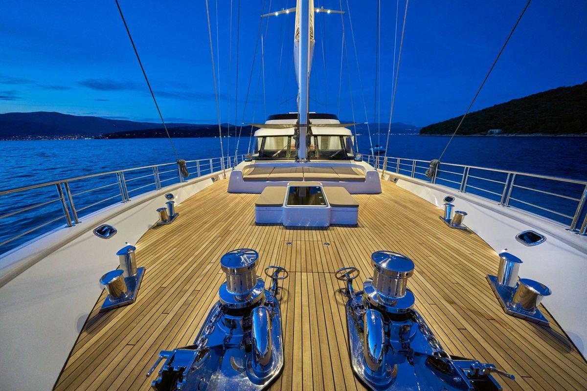 luxury yacht forward deck with teak planking and stainless windlasses at twilight