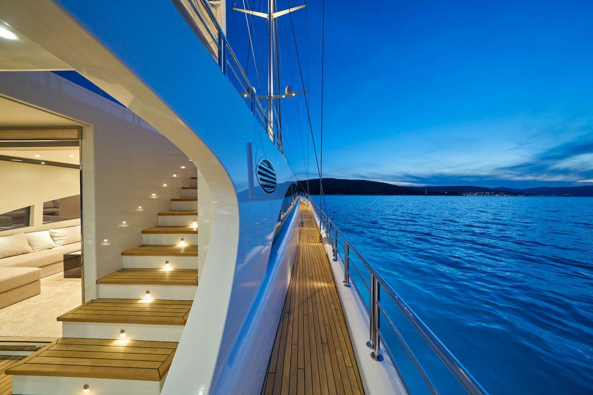 luxury yacht port deck with teak planking and illuminated salon entrance at twilight
