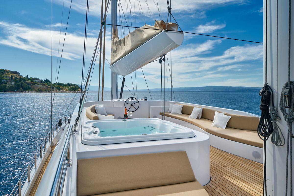 Luxury sailing yacht aft deck featuring white jacuzzi surrounded by cushioned seating