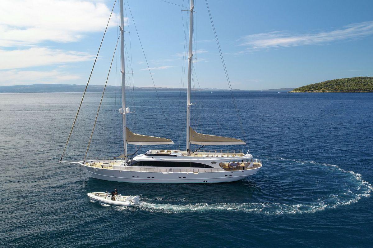 luxury white sailing yacht anchored in blue Mediterranean waters with tender
