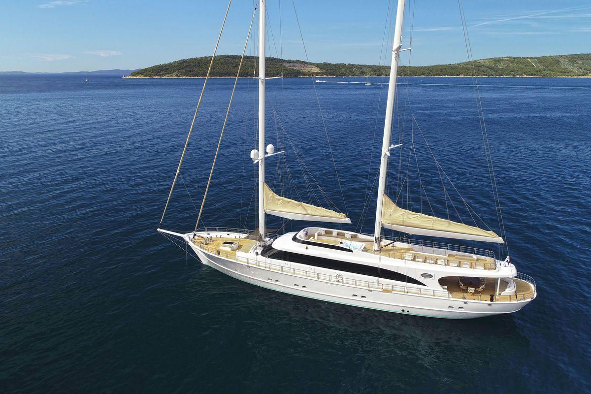 White luxury sailing yacht with two masts anchored in crystal clear turquoise bay