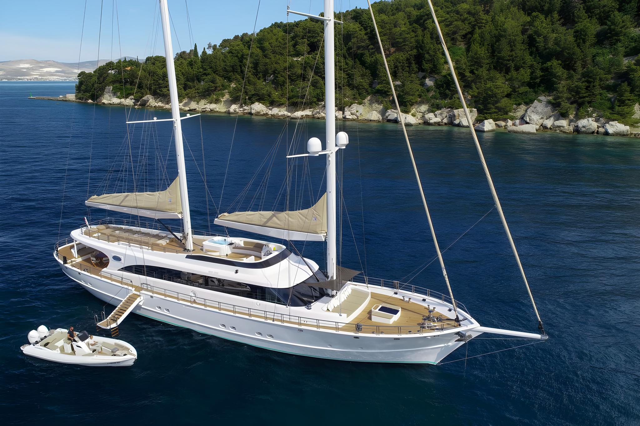 White luxury sailing yacht with two masts anchored near forested Mediterranean coastline