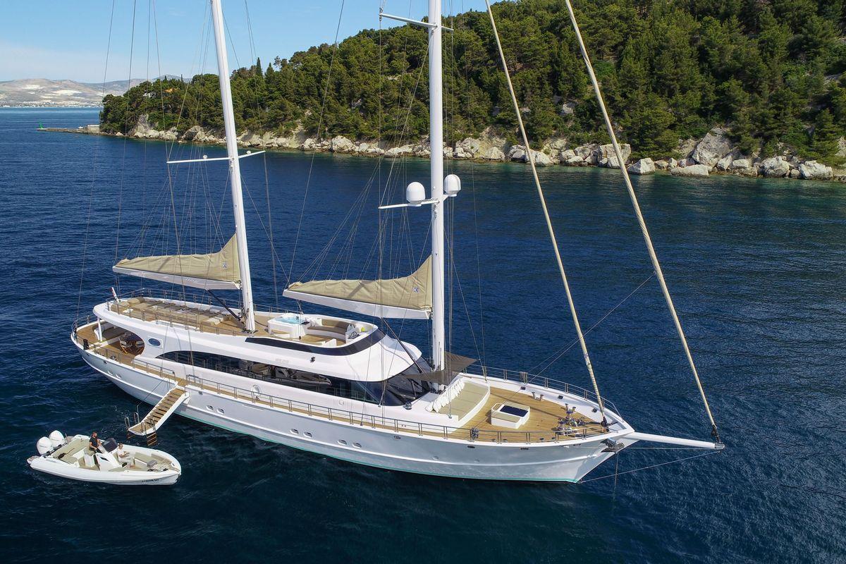 White luxury sailing yacht with two masts anchored near forested Mediterranean coastline