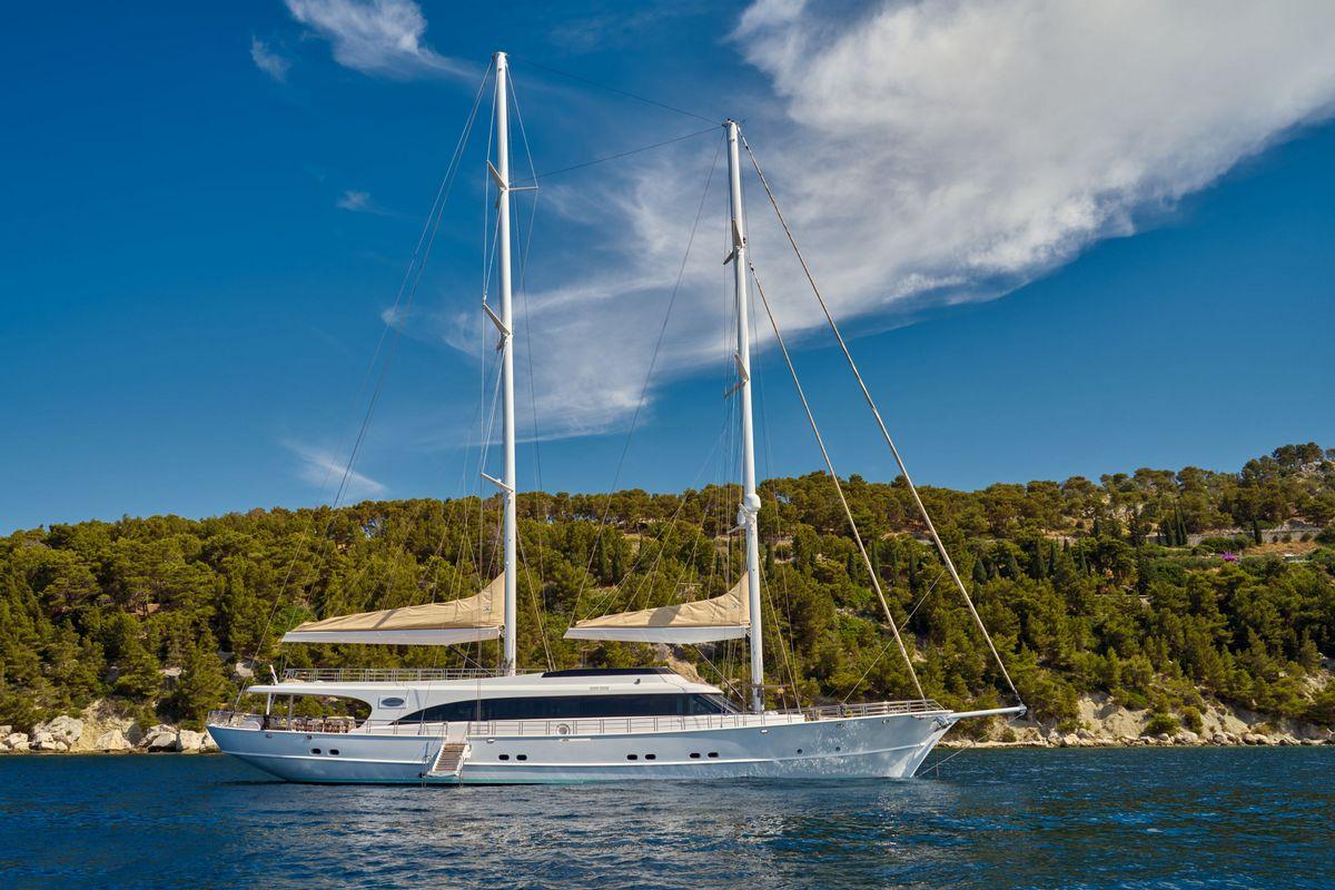luxury white sailing yacht with two masts anchored near forested coastline