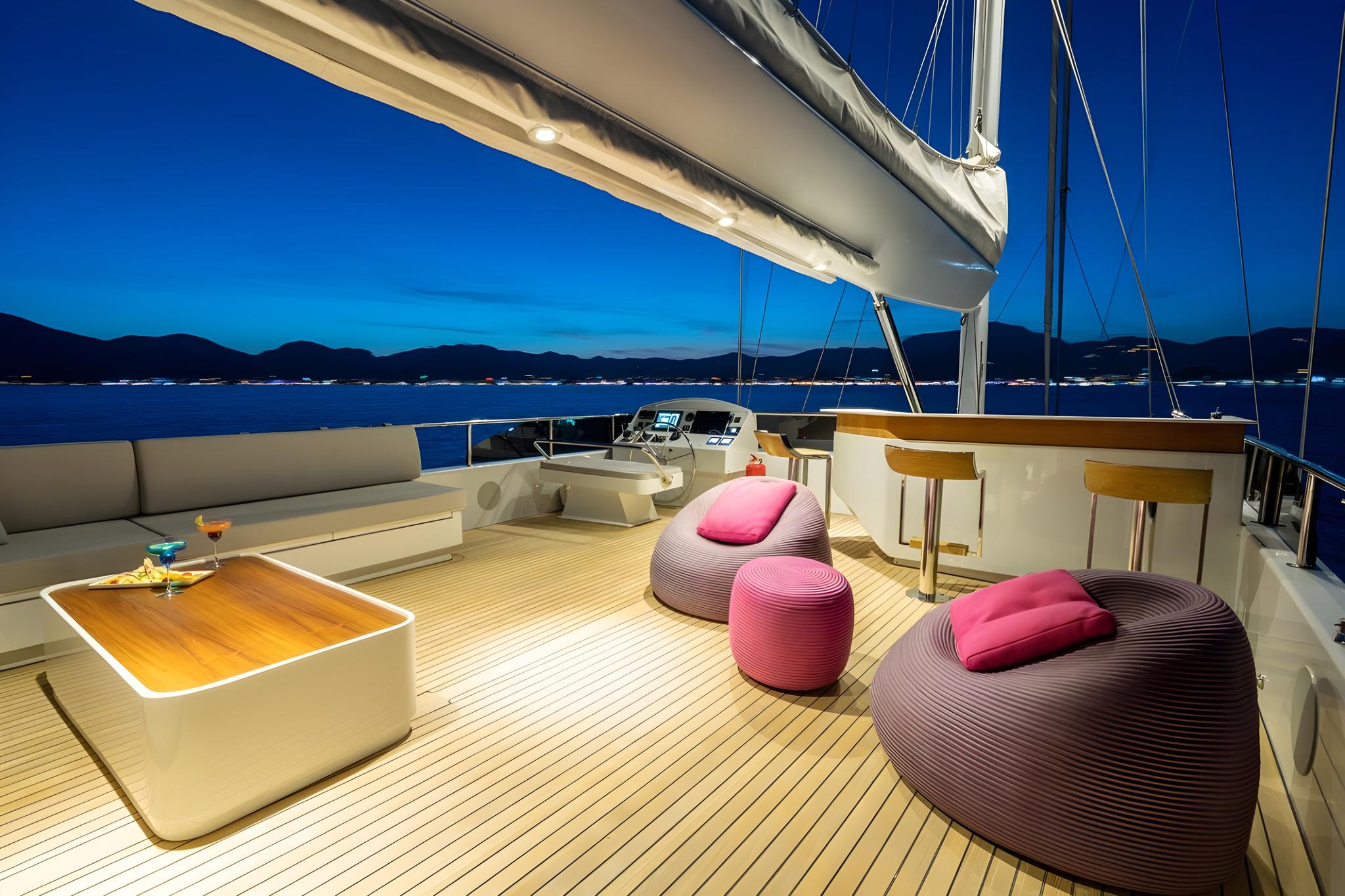 yacht aft deck with curved sofa seating, pink bean bags, teak bar with stools at twilight